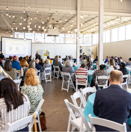 Photo of a crowd of people sitting at tables and listening to a presentation at the Disability Inclusion Breakfast.