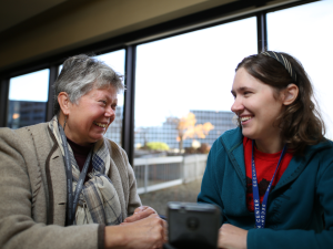 A photo of two women sitting in an office and talking to one another.